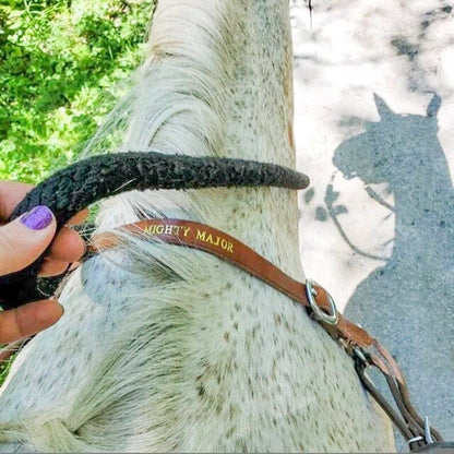 personalized leather wither strap shown on a grey horse holding up a breast collar on a trail ride. Brown leather strap with nickel hardware and gold text in the center reading Mighty Major.